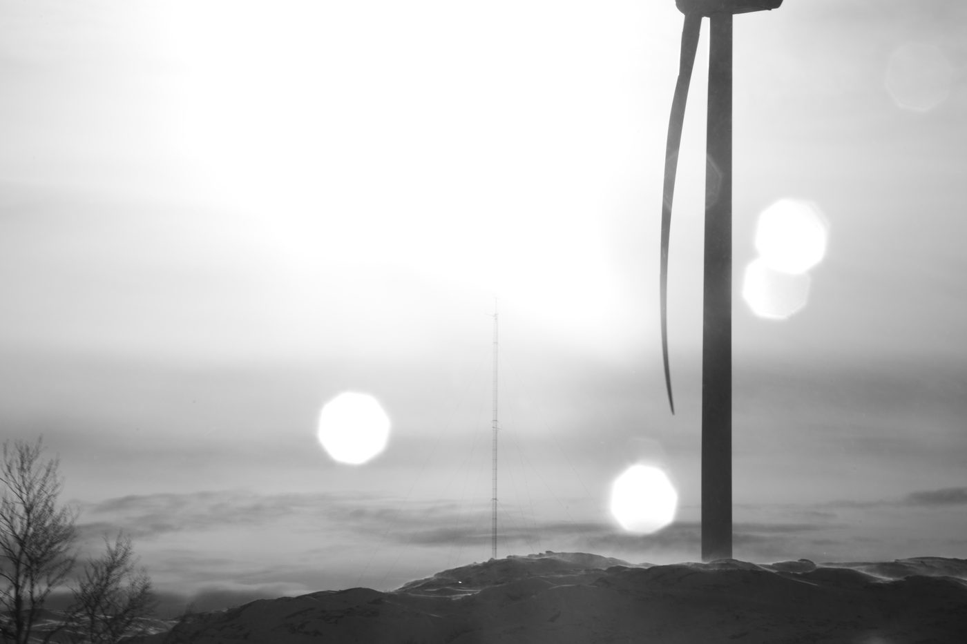 A wind turbine and a lattice meteorological mast silhouetted on a misty ridge