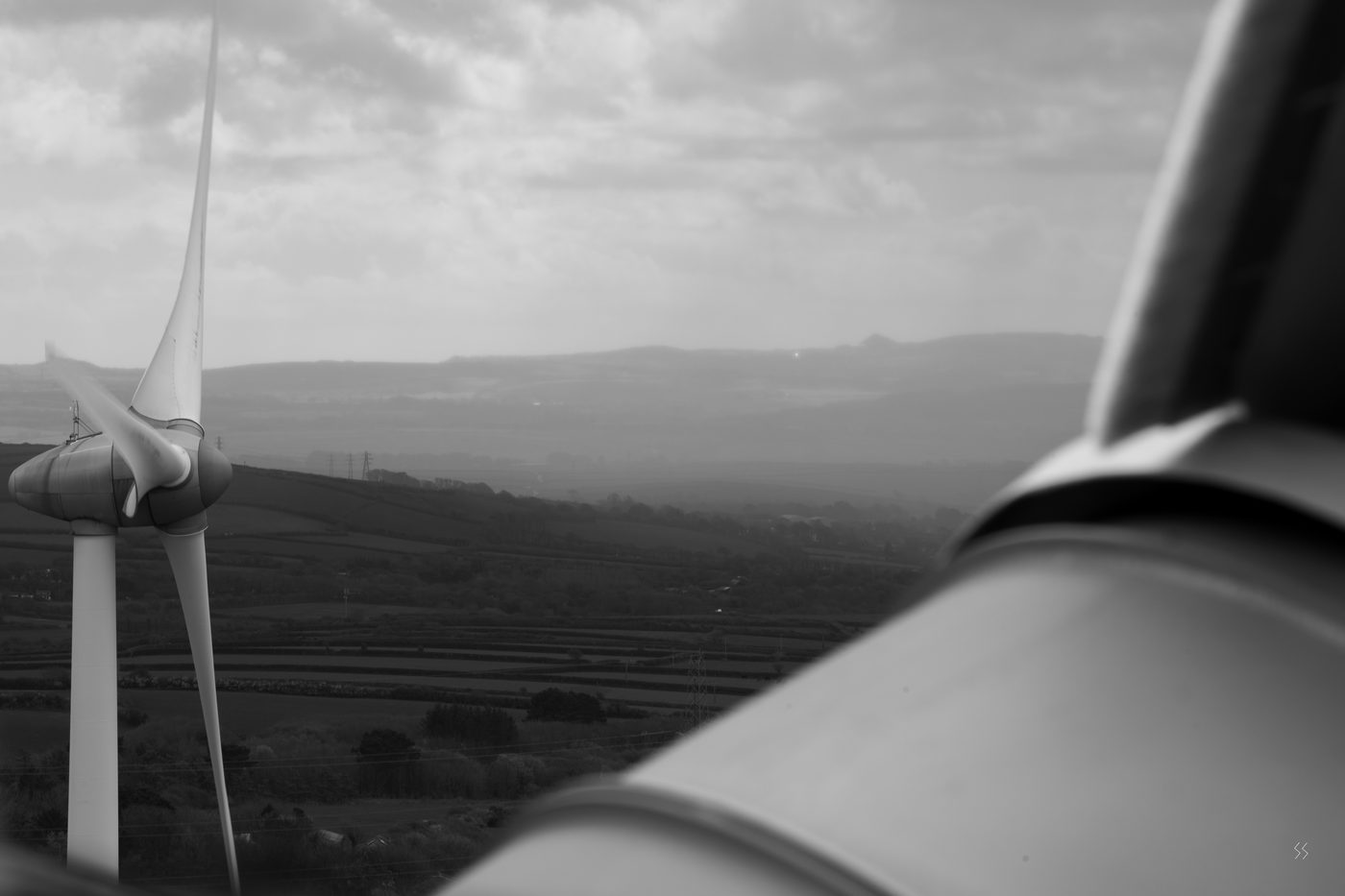 The view from a wind turbine nacelle across farmland, a second turbine in the middle distance
