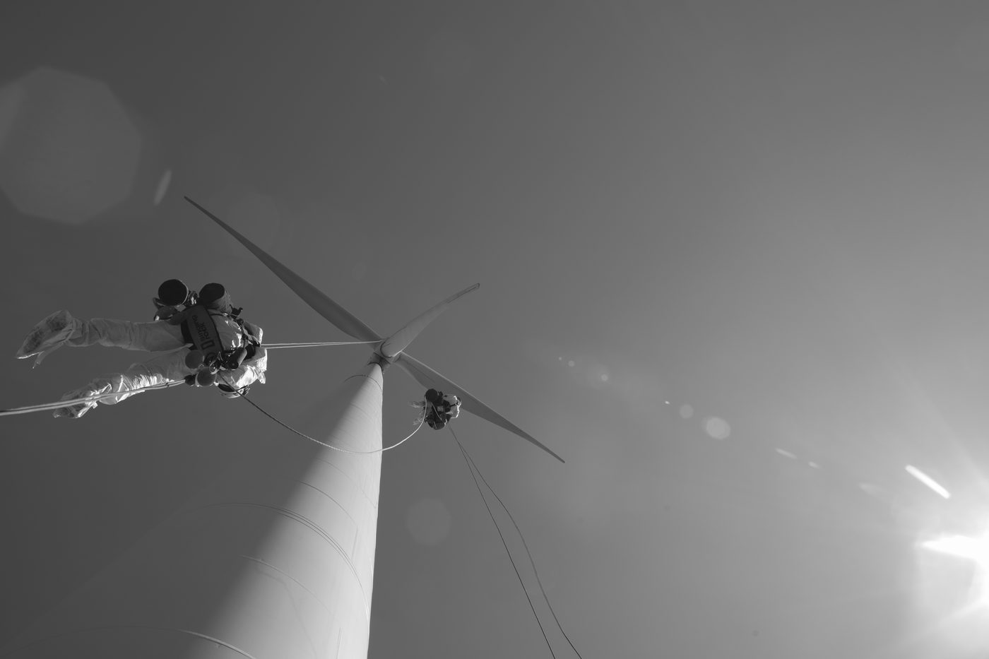 Looking up at a wind turbine from the base, two rope access technicians working at the hub with ropes hanging beneath them